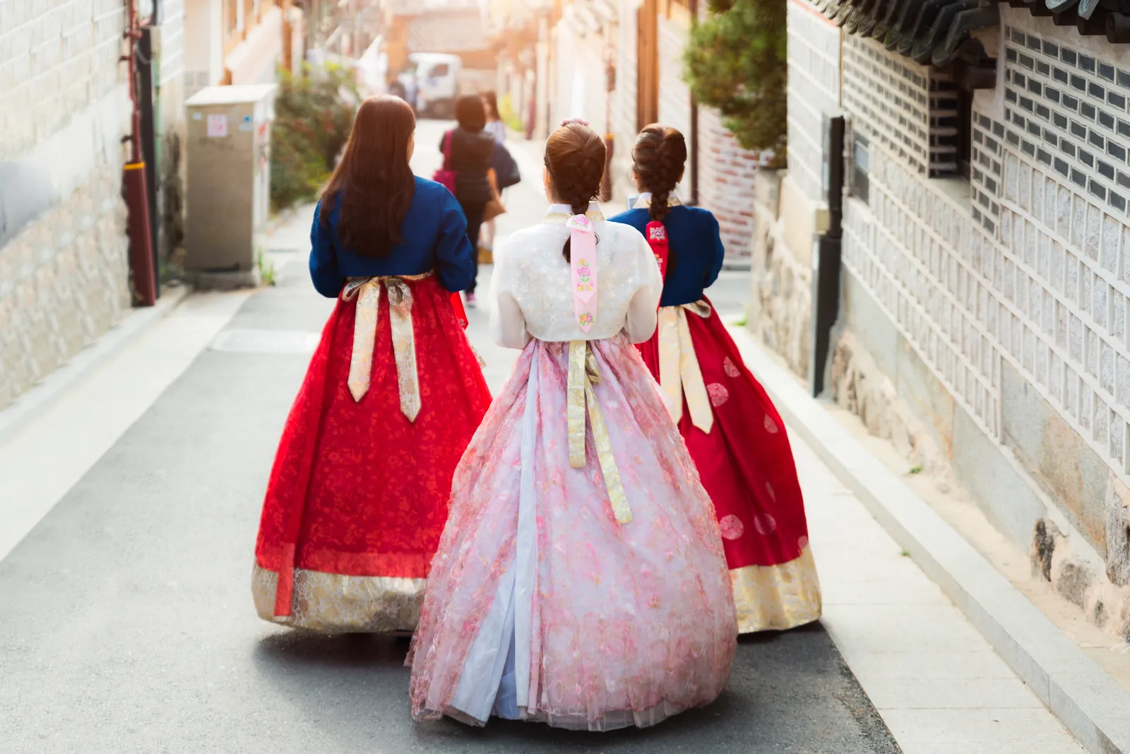 Three women in hanbok walking up a narrow lane between hanok houses