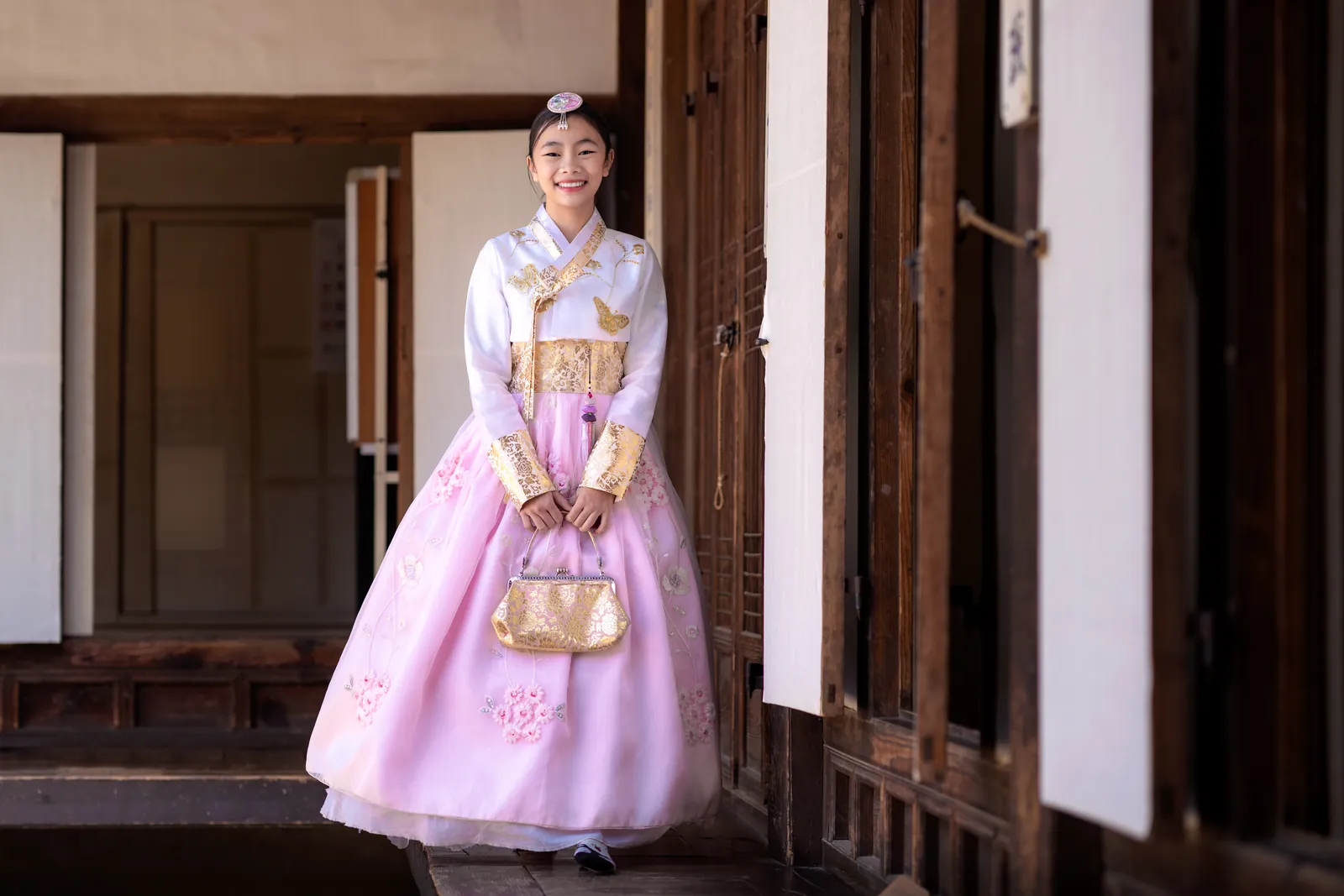 A woman in a pink hanbok with gold trim standing in a wooden doorway